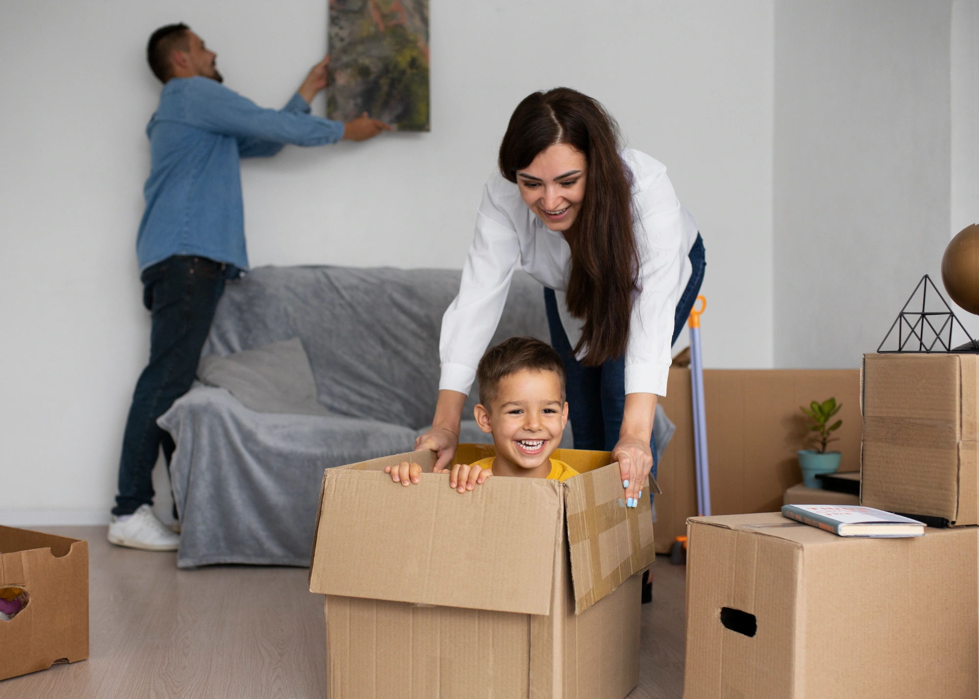 Young boy playing in cardboard box with his mother, while father unpacks